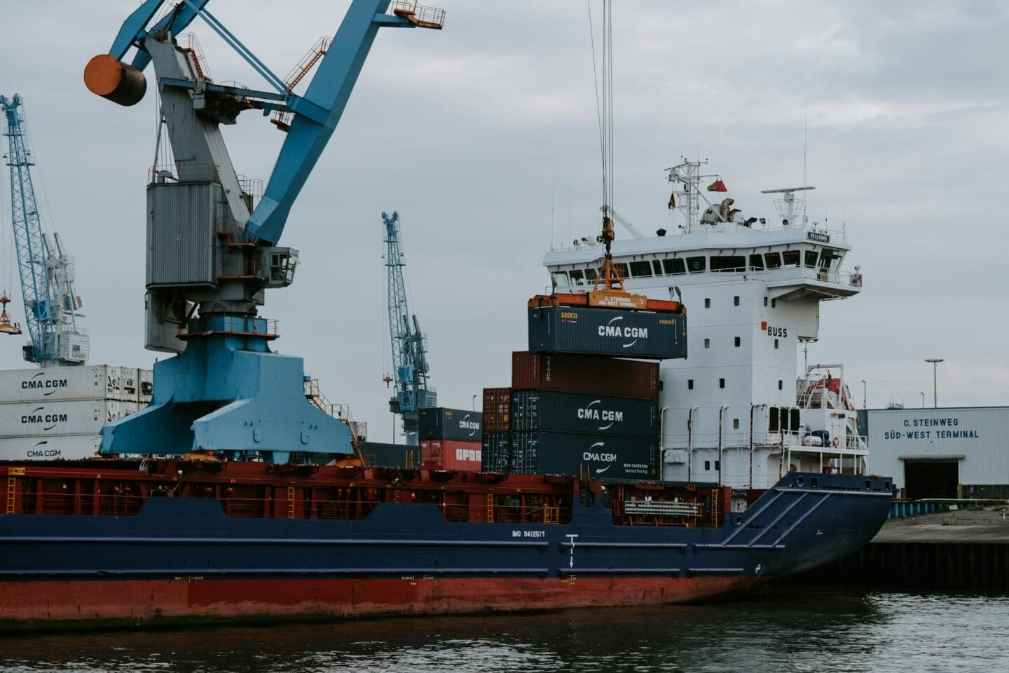 A blue and red cargo ship docking at the port